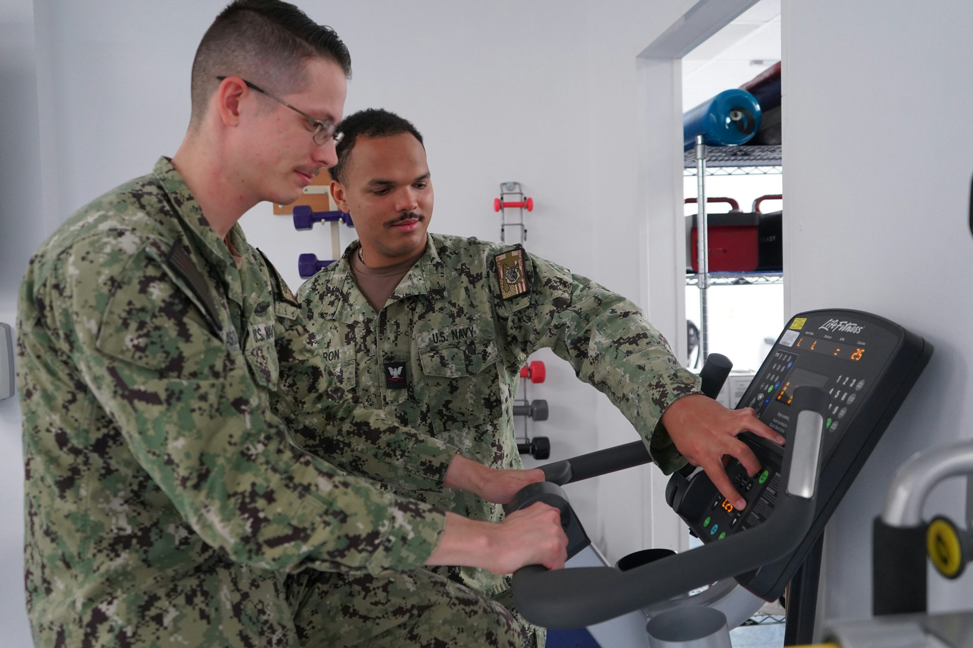 Two sailors adjusting treadmill console