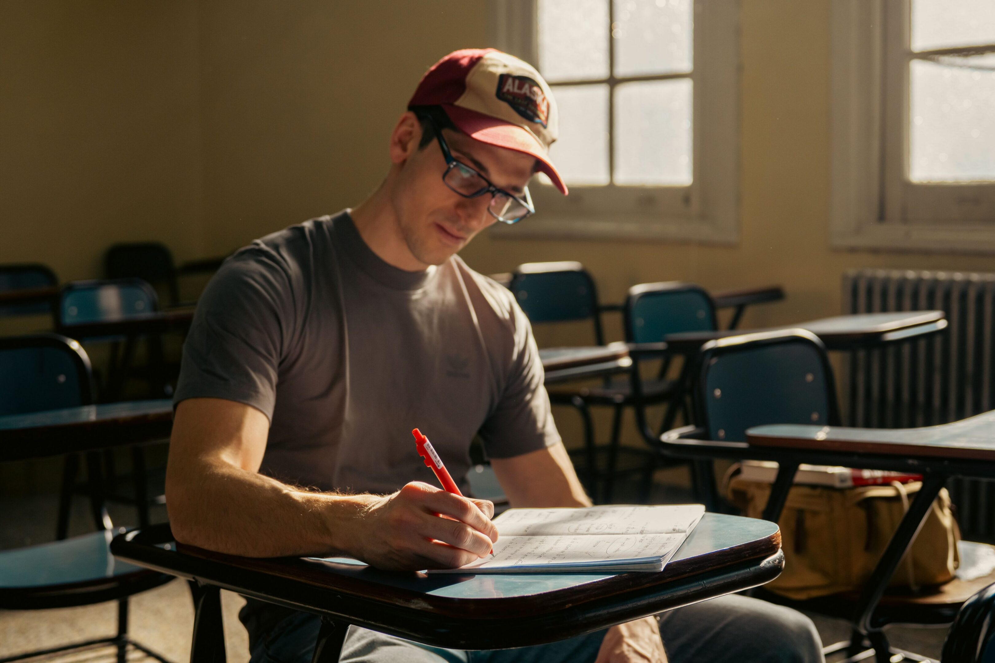 Student writing with red pen in classroom